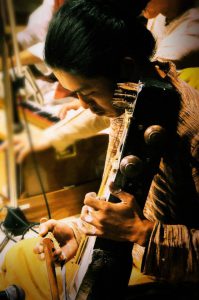 サーランギ奏者 オカダケンシン2009年、聖地ベナレスにてShivendra Mishra氏、Fiyaz Ali Khan氏の元、弓奏楽器サーランギの修行を始める。 以降毎年渡印。2014年よりデリーにてMoradabad流派の巨匠Ustad Ghulam Sabir Khan氏に師事。 北インド古典音楽をはじめ、様々なジャンルのアーティストとのセッションも行いながら田畑を営み薪で暮らす。岡山在住。